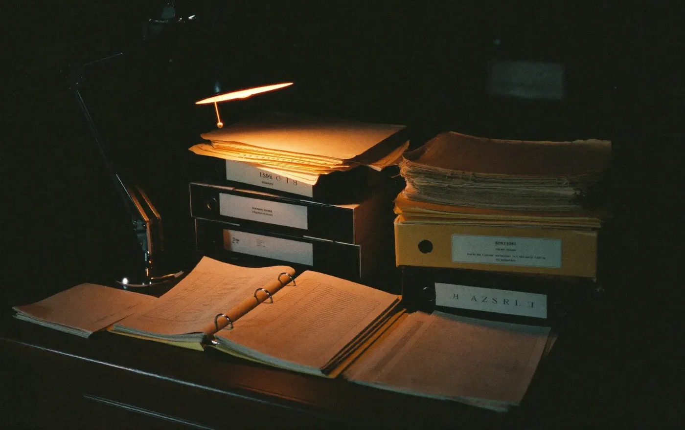 Stacks of aged folders and service reports on a desk in low warm light